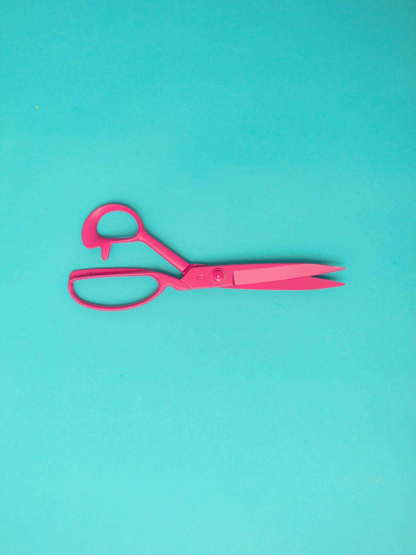 Pink tailor's shears on a turquoise surface